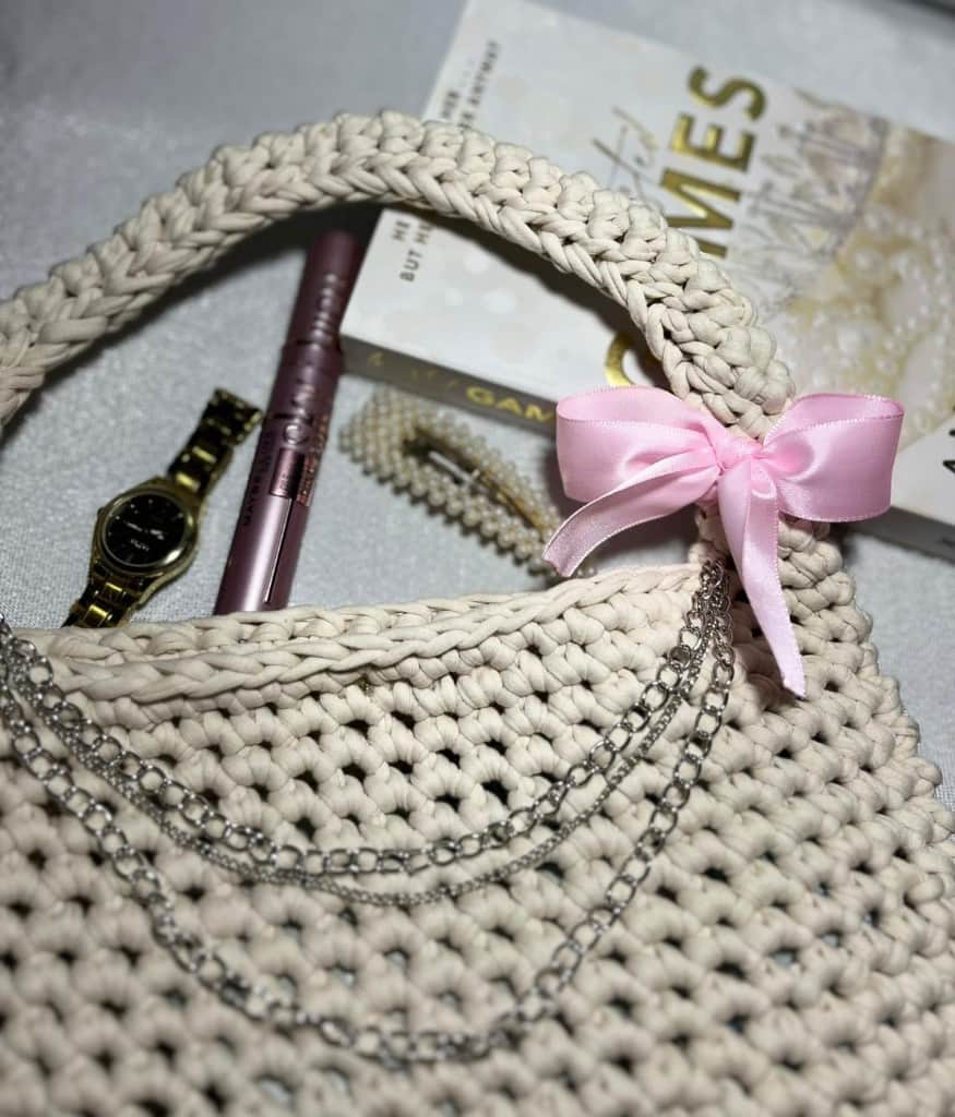 Tamborēta bēša rokassoma ar rozā lentīti un sudraba ķēdīti.