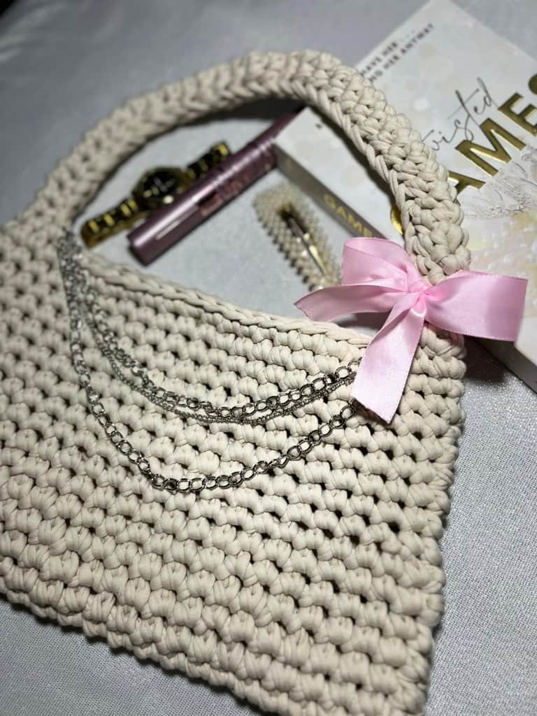 Tamborēta bēša rokassoma ar rozā lentīti un sudraba ķēdīti.